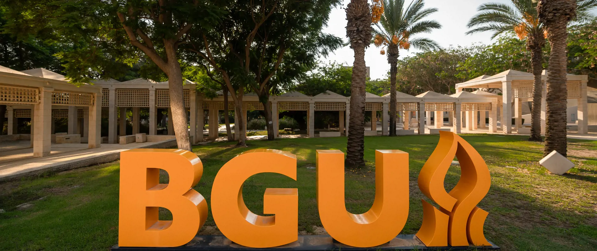 Outdoor garden with palm trees, orange letters spelling "BGU", and a grassy lawn.